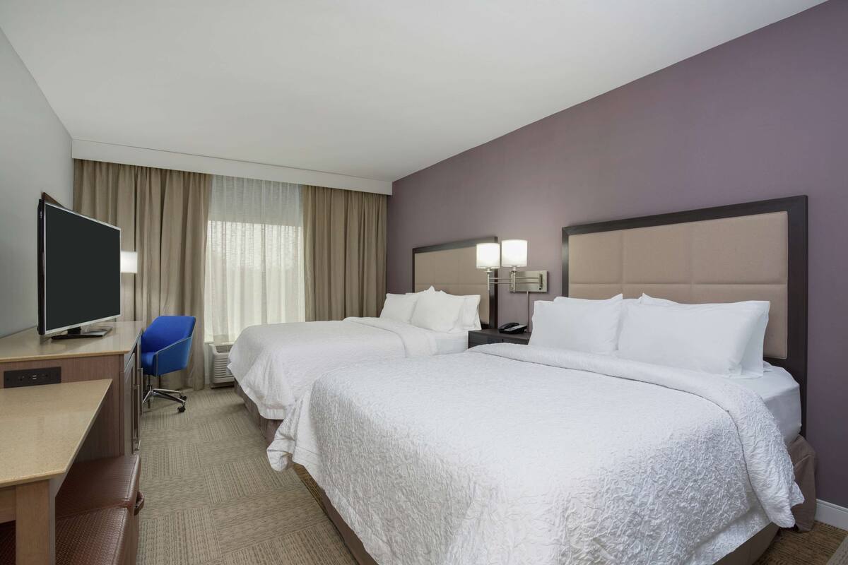 A hotel room with two beds, a desk, a TV, and a chair.