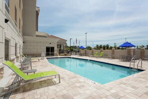 A swimming pool with lounge chairs and umbrellas, surrounded by a building with a tiled exterior. - Hampton Inn & Suites Jacksonville / Orange Park (Orange Park)
