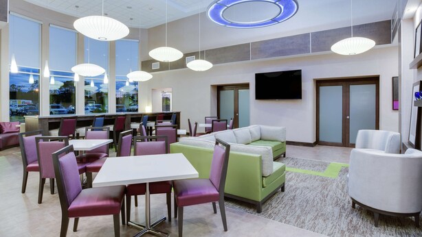 A modern hotel lobby with seating areas, tables, and a large TV screen. - Hampton Inn & Suites Jacksonville / Orange Park (Orange Park)