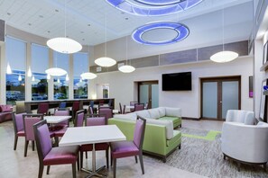 A modern hotel lobby with seating areas, tables, and a large TV screen. - Hampton Inn & Suites Jacksonville / Orange Park (Orange Park)