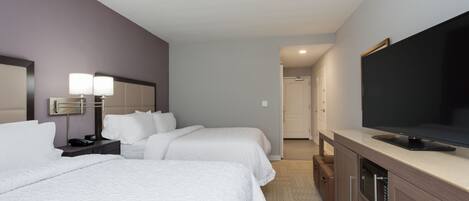 Una habitación de hotel con dos camas, televisión, mesita de noche con lámpara y armario.