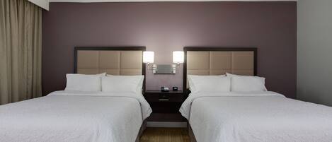 A hotel room with two beds, a nightstand, and a mirror between the beds.