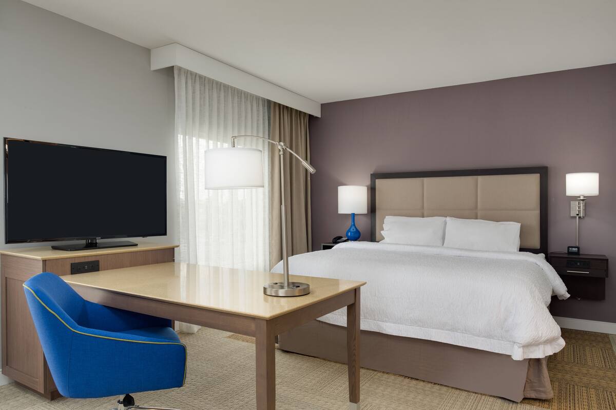 A hotel room with a bed, a desk with a chair, a television, and two bedside lamps.