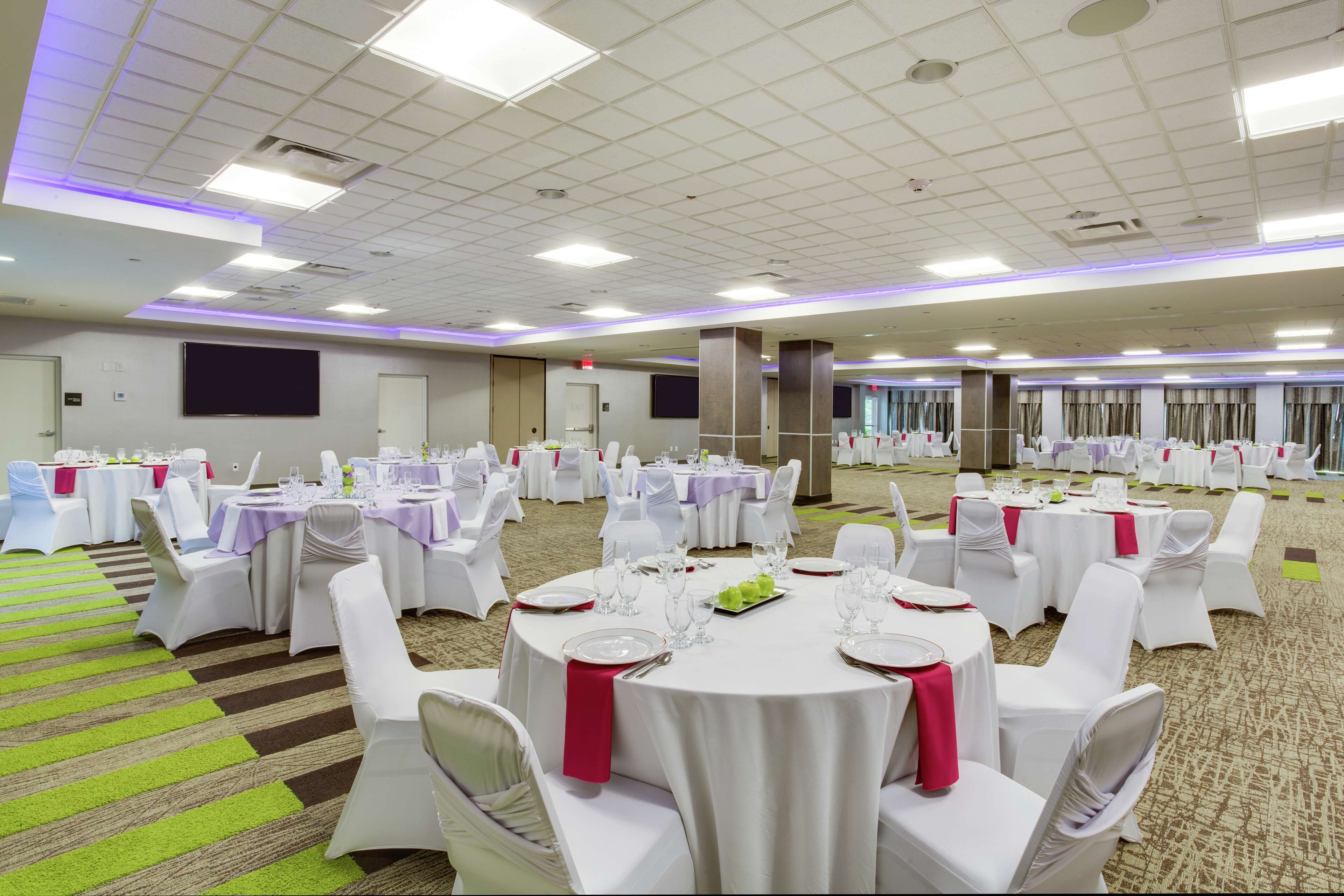 Een ruime balzaal met ronde tafels voor evenementen, witte stoelen en een vloerbedekking.