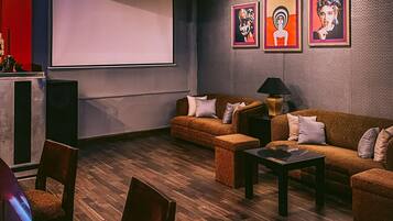 Una habitación con piso de madera, dos sofás, una mesa de centro y una pantalla de proyector, además de tres obras de arte enmarcadas en la pared.