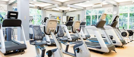 A gym with multiple treadmills and elliptical machines, large windows with natural light, and a clean, modern design.