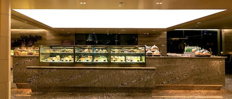 A modern hotel lobby with a marble reception desk, a glass display case with various items, and a large illuminated ceiling.