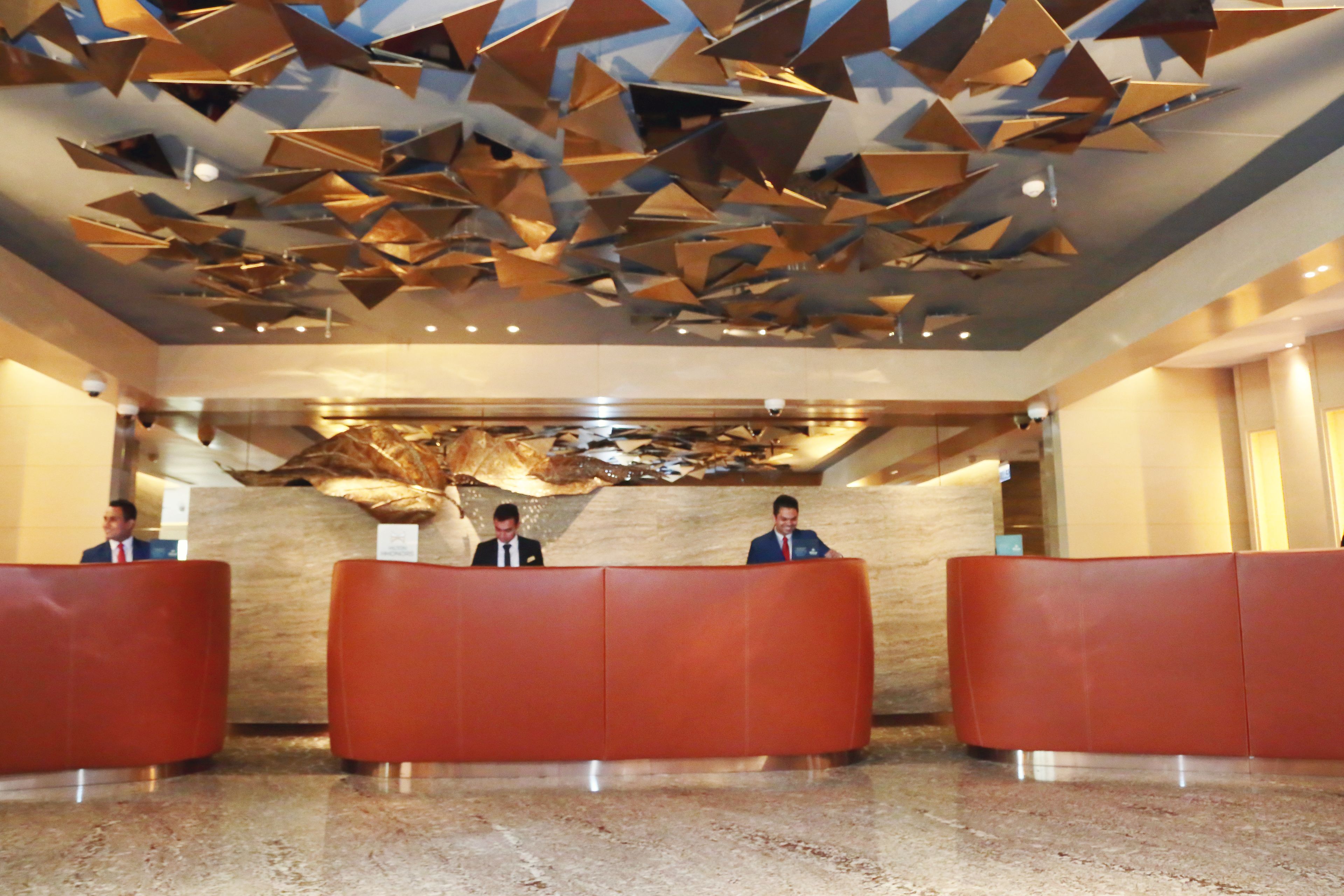 A reception area with three red reception desks, a modern ceiling design, and a marble floor.
