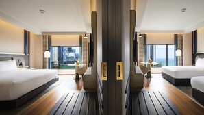 Habitación de hotel con dos camas, una mesita, sillas y vista a la ciudad.