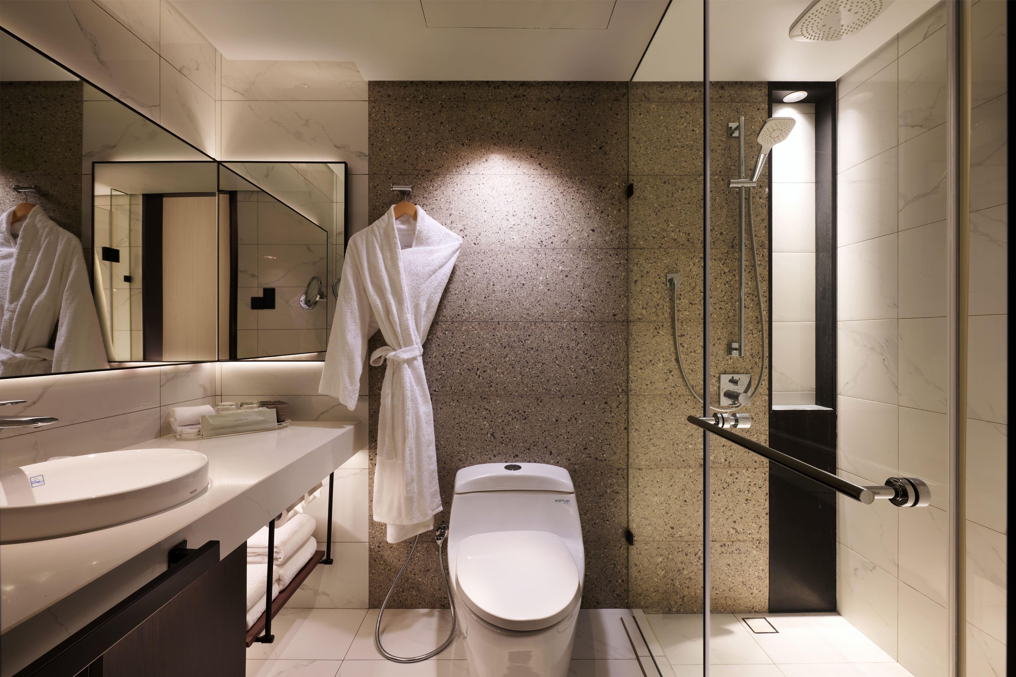 A modern bathroom with a marble vanity, a toilet, a glass shower enclosure, and a robe hanging on a rack.