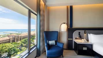 A hotel room with a large window, a blue armchair, a bedside table with a lamp, and a bed.