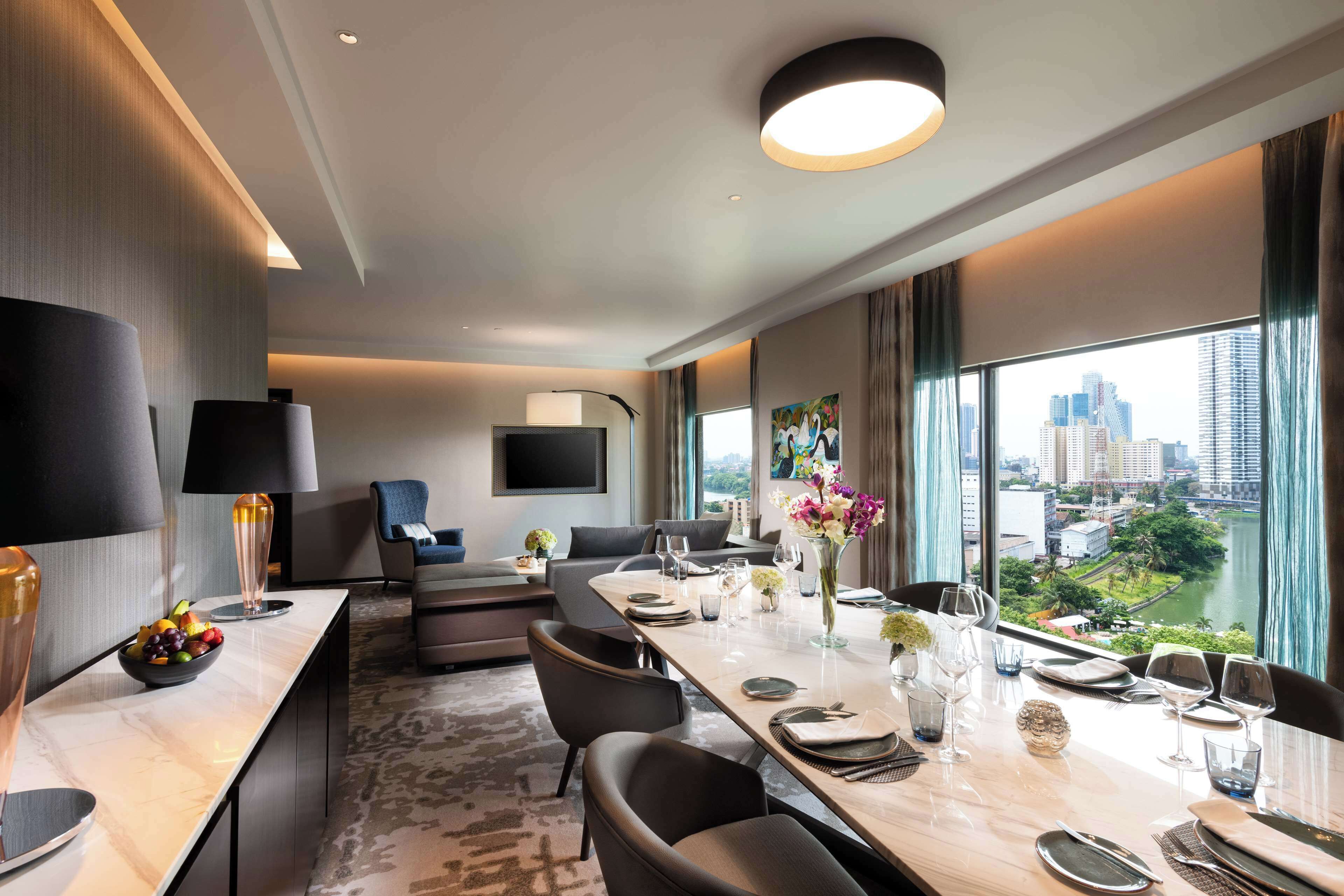 A modern hotel room with a dining area, a flat-screen TV, and a city view.
