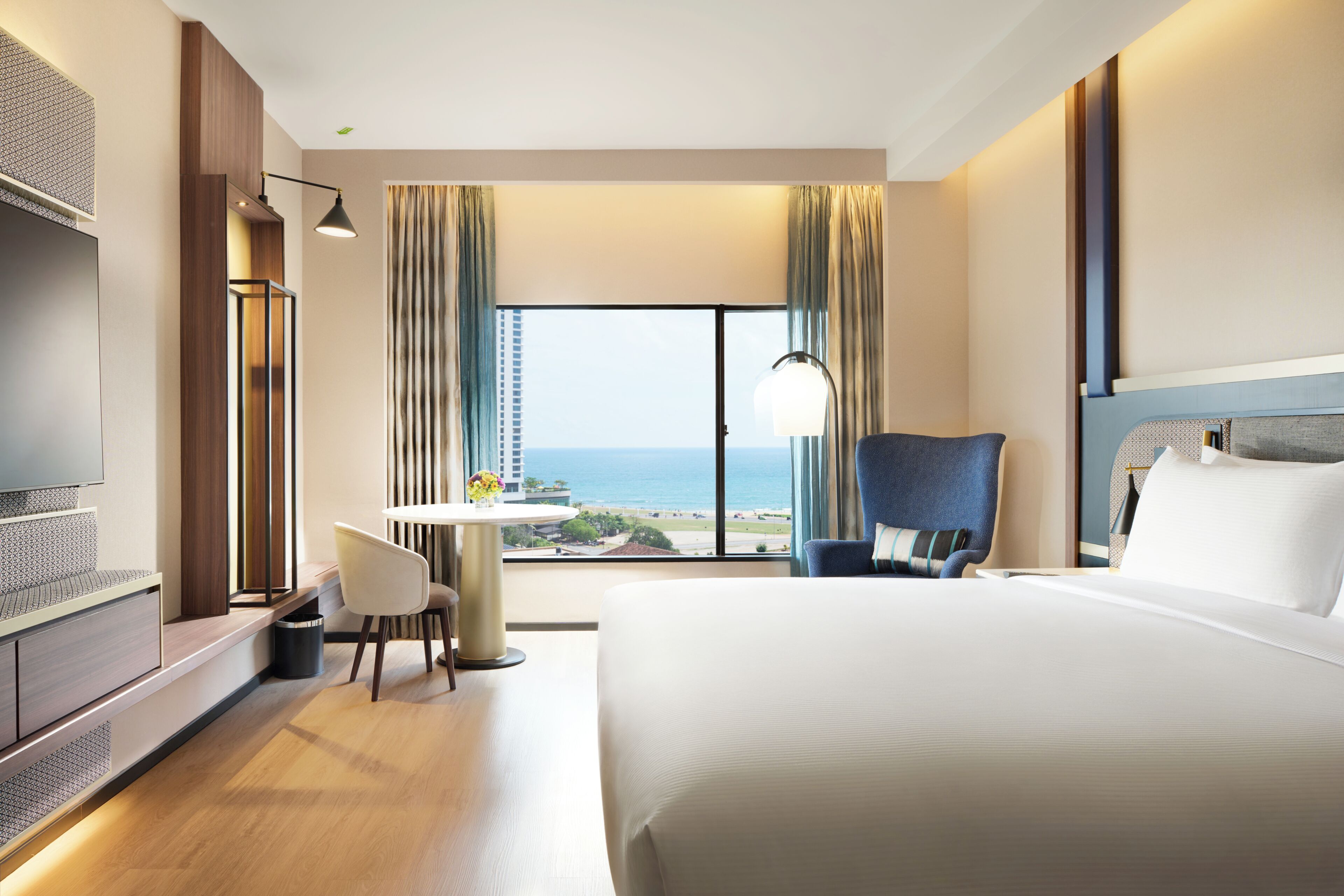 Habitación de hotel con una cama grande, un escritorio, una silla, un televisor y vista al océano.