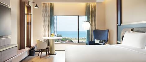 Habitación de hotel con una cama grande, un escritorio, una silla, un televisor y vista al océano.