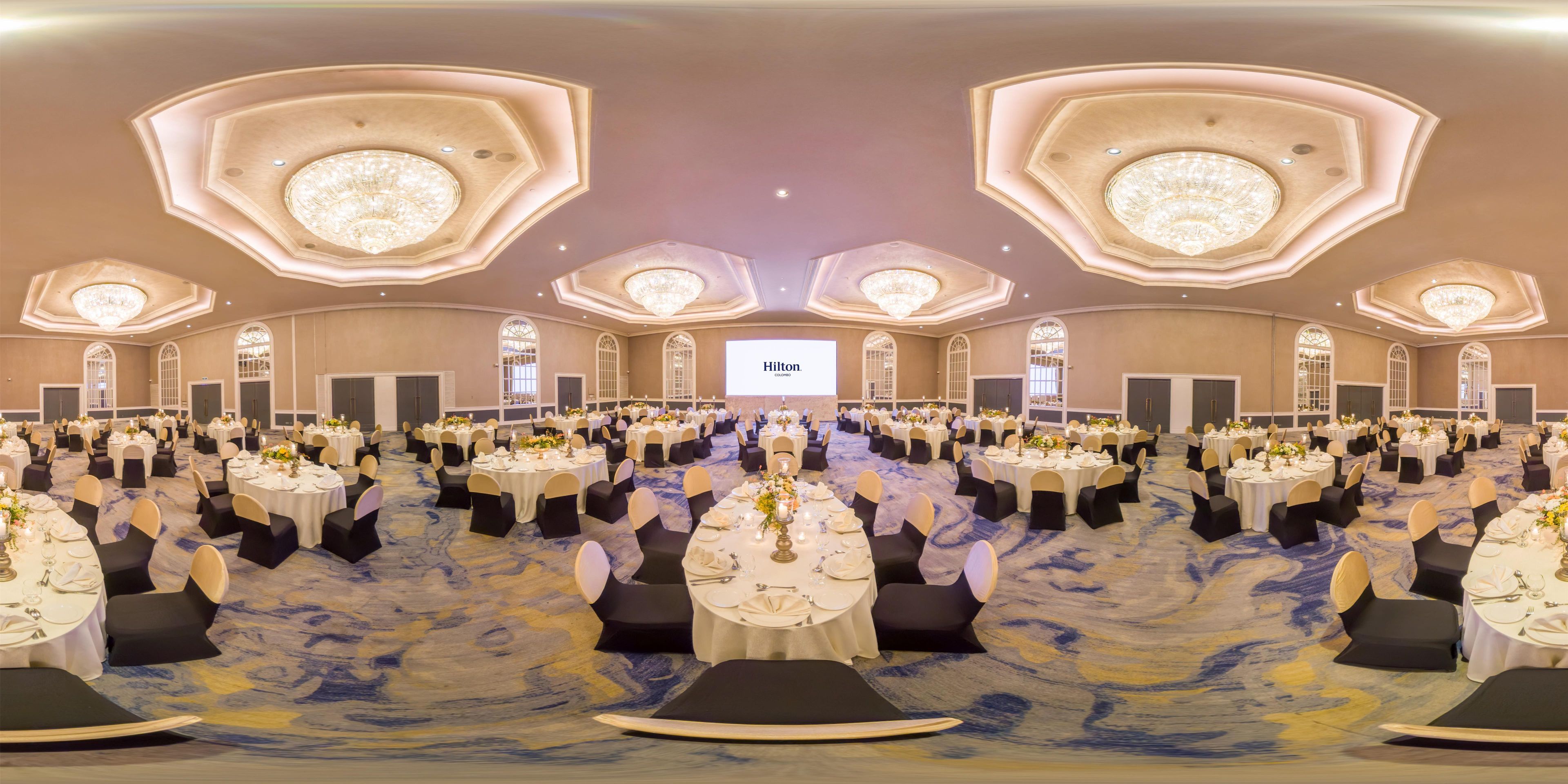 Un gran salón de banquetes con mesas redondas, sillas negras y candelabros.