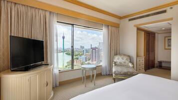 Une chambre d’hôtel avec un grand lit, un téléviseur posé sur un meuble, une chaise, une petite table et une vue sur le paysage urbain par une grande fenêtre.