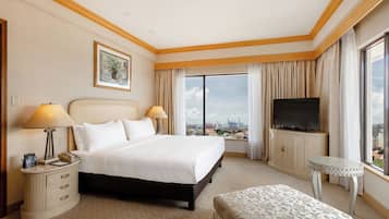 A hotel room with a large bed, a television, a desk with a lamp, and a view of the city.