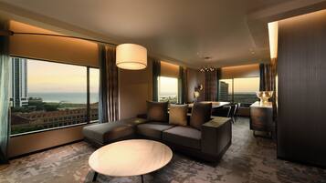 A modern hotel room with a sectional sofa, a round coffee table, and large windows offering a city view.