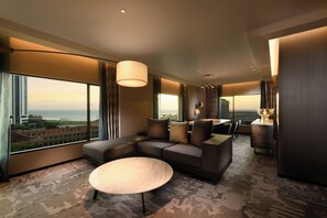 Habitación de hotel moderna con sofá modular, una mesa de centro redonda y grandes ventanales con vistas a la ciudad.