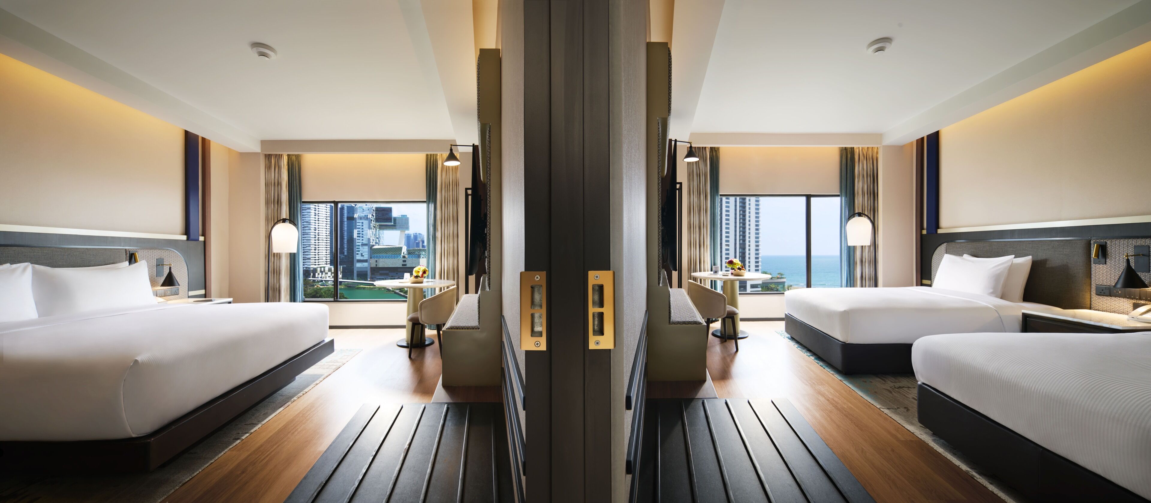 Ein Hotelzimmer mit zwei Betten, Blick auf die Stadtlandschaft und einem Essbereich mit Tisch und Stühlen.