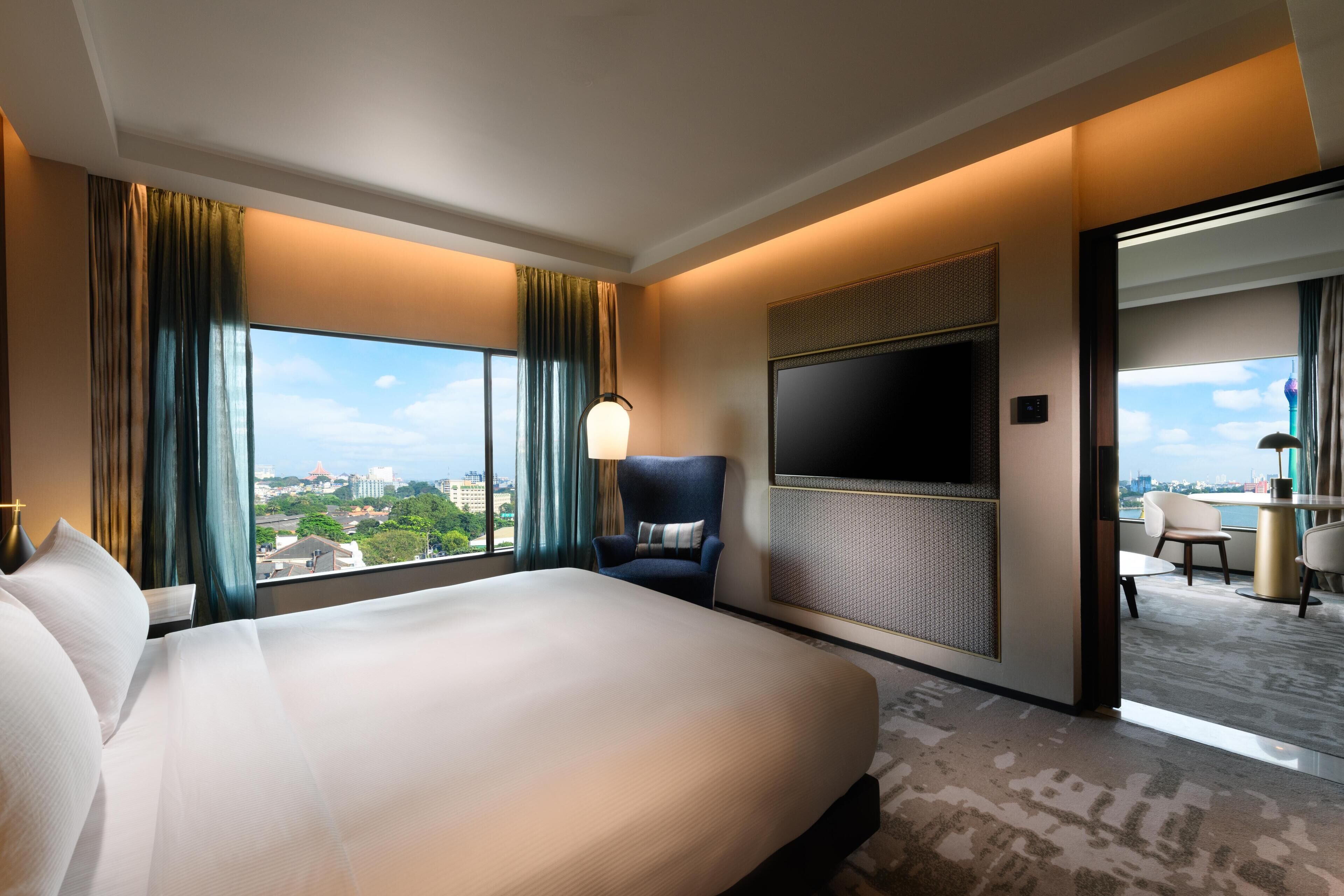 A hotel room with a large bed, a TV mounted on the wall, and a view of the city through the window.