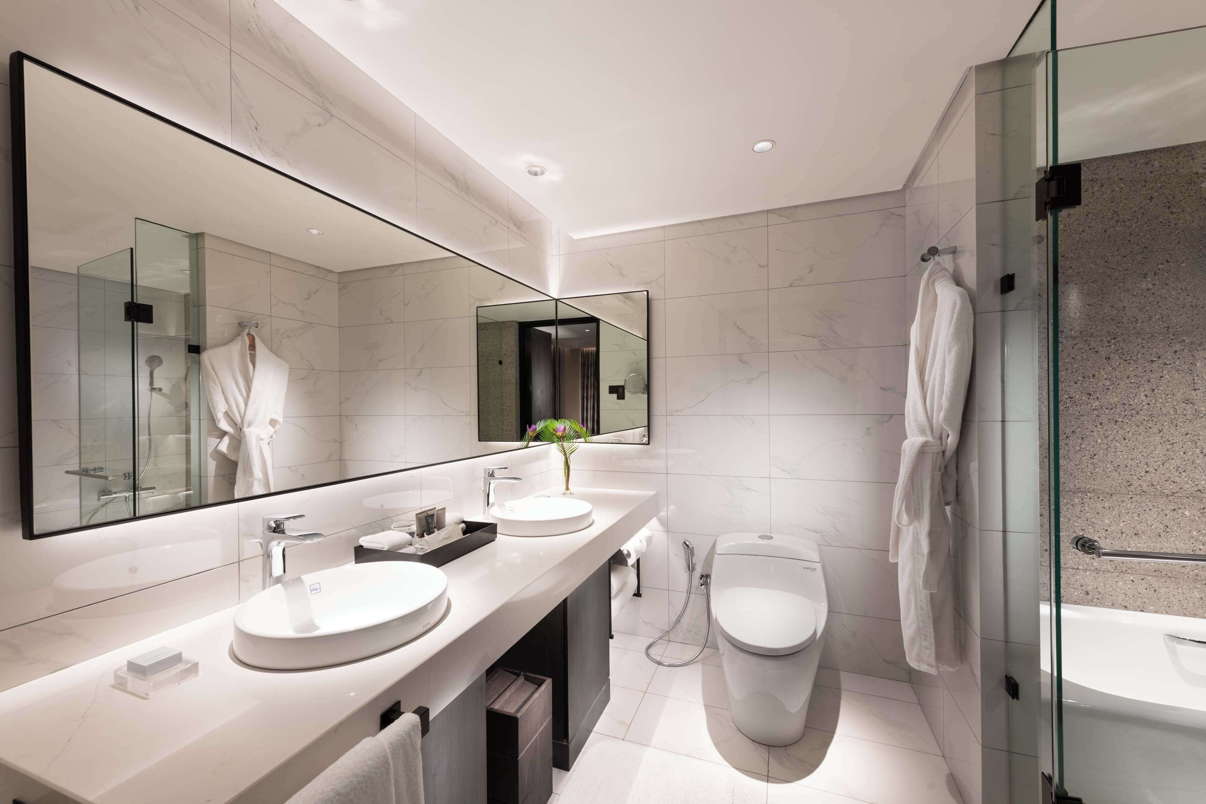 A modern bathroom with two sinks, a toilet, a shower, and a large mirror.