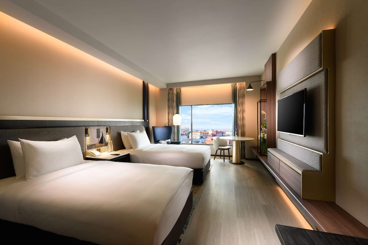 Ett hotellrum med två sängar, ett skrivbord, en TV och utsikt över staden.