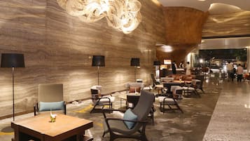 A modern hotel lobby with marble walls, contemporary furniture, and a large decorative light fixture.