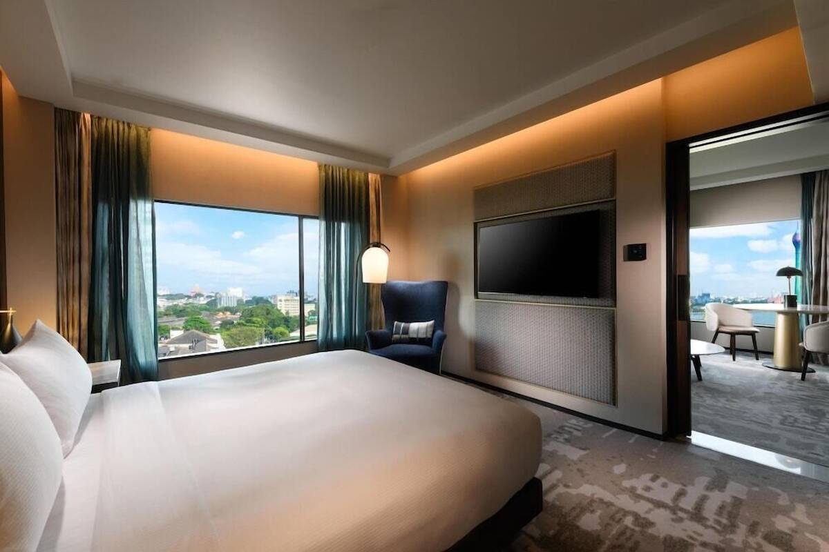 Ett hotellrum med en stor säng, en tv som är monterad på väggen och utsikt över stadsbilden genom fönstret.