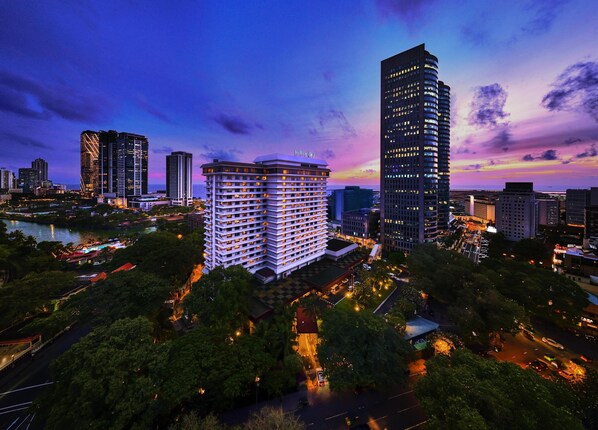 A high-rise hotel with a modern design, surrounded by lush greenery and a river.
