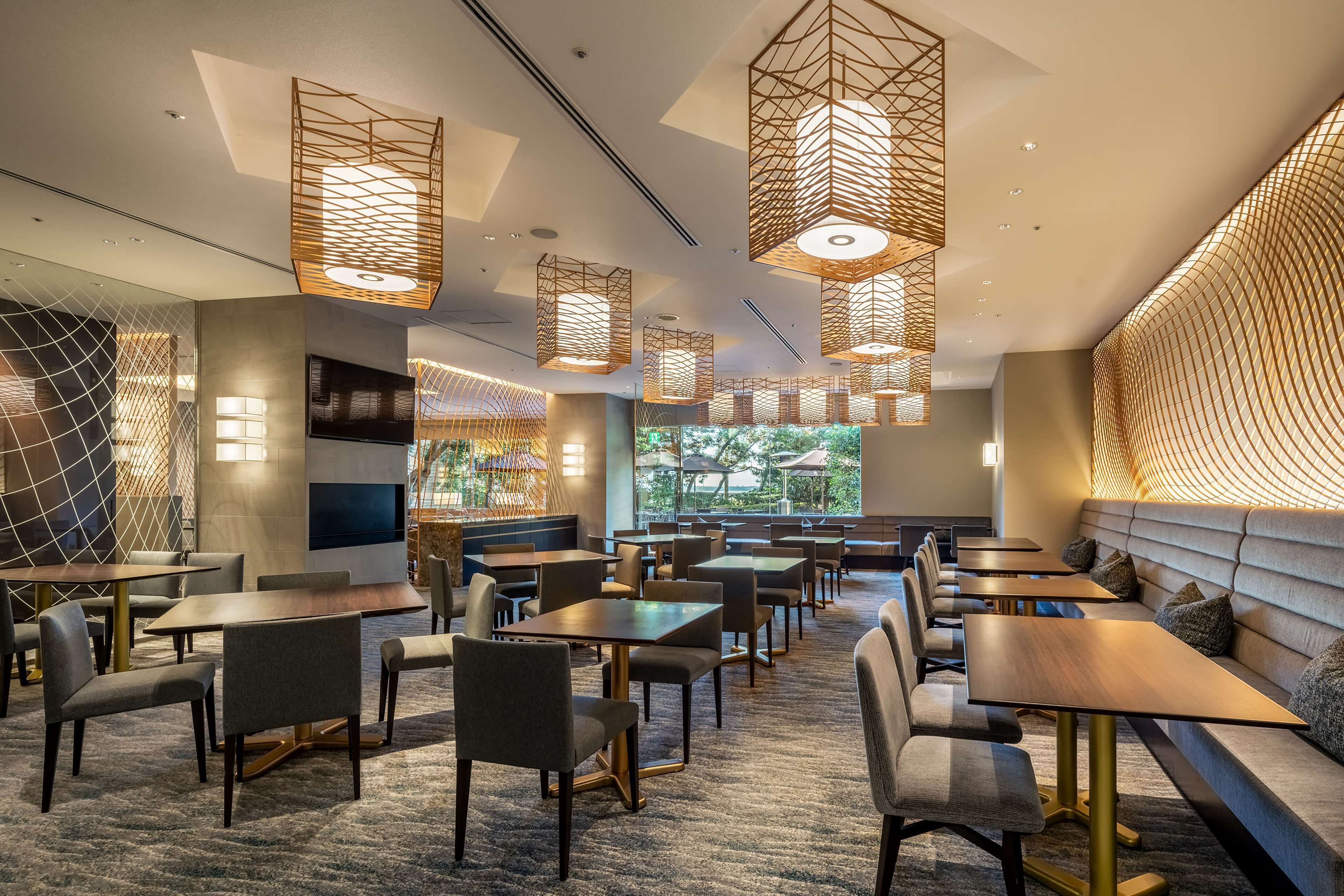 En moderne restaurant med flere siddeområder, herunder borde og båse, samt et stort tv på væggen.