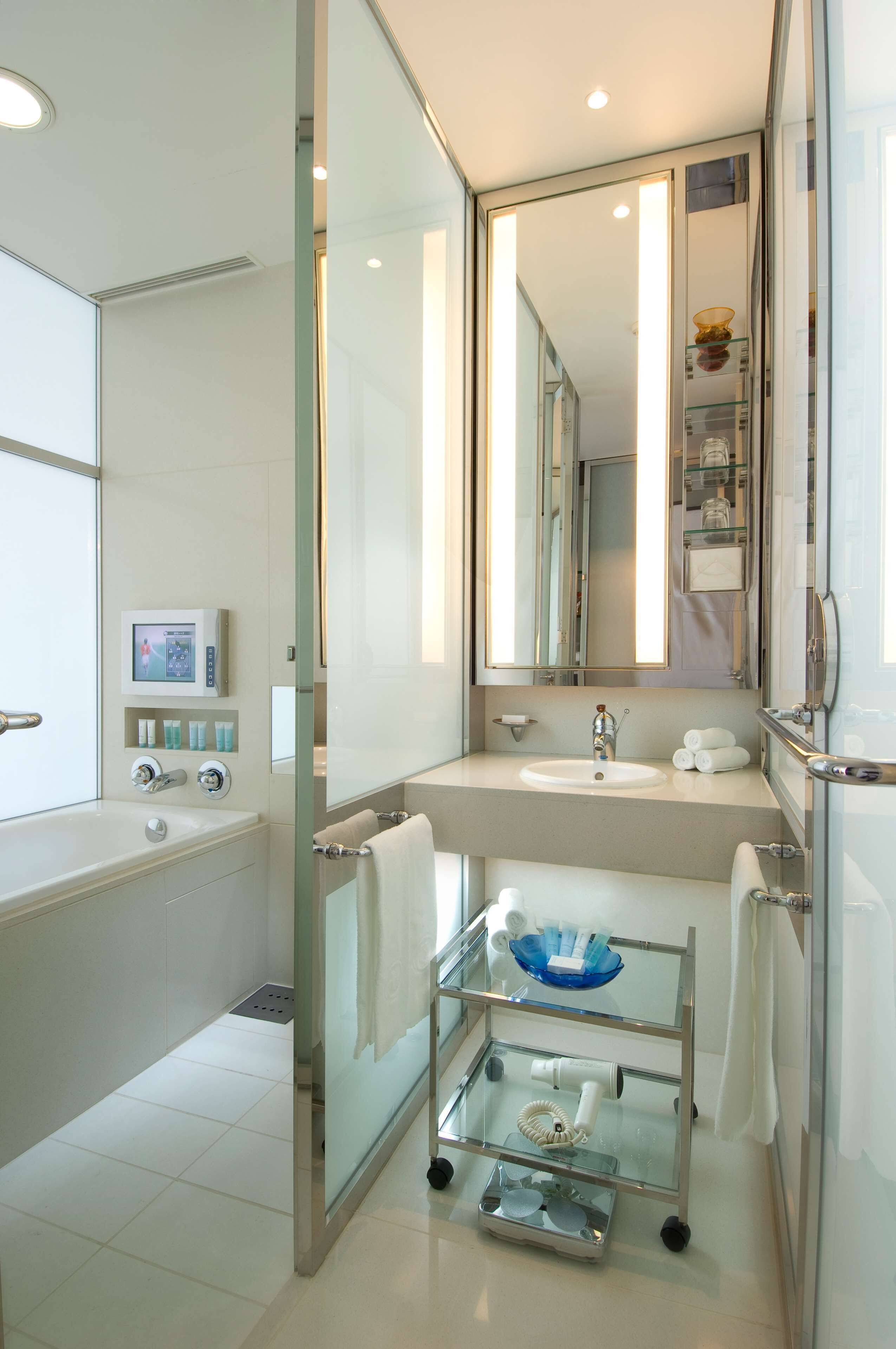 A modern bathroom with a glass-enclosed shower, a vanity with a sink, and a glass cart with toiletries.