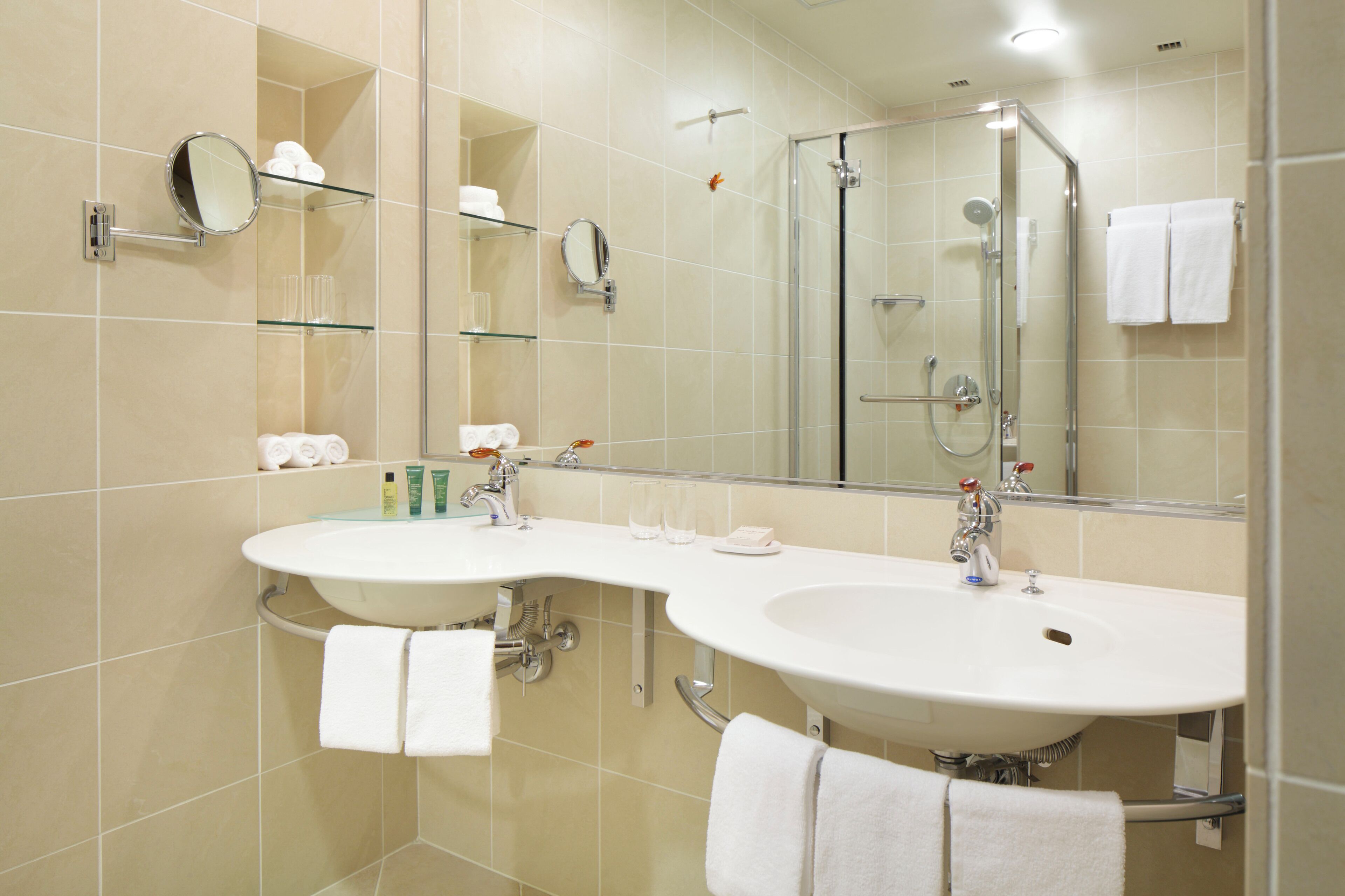 A modern bathroom with two sinks, a glass shower enclosure, and a large mirror.