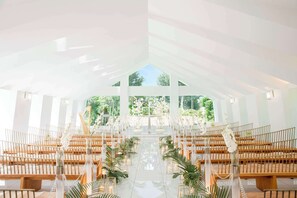 An indoor venue with a high ceiling, wooden pews, and a central aisle.