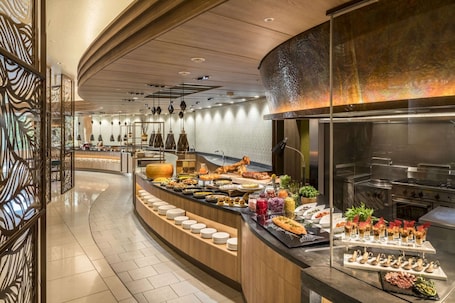 A buffet area with a variety of food items, a long counter with plates, and a kitchen area in the background.