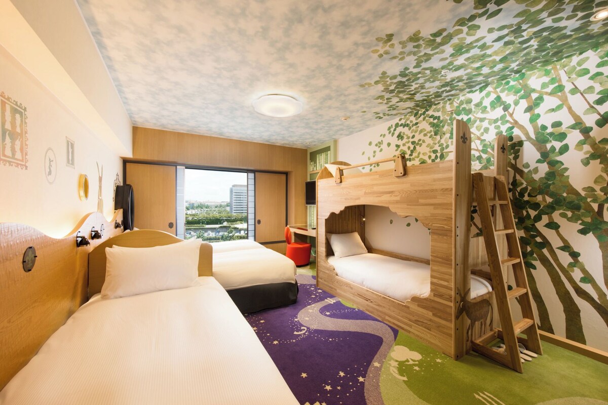A hotel room with two beds, a wooden bunk bed, a ladder, a view of the city, and a wall with a tree mural.