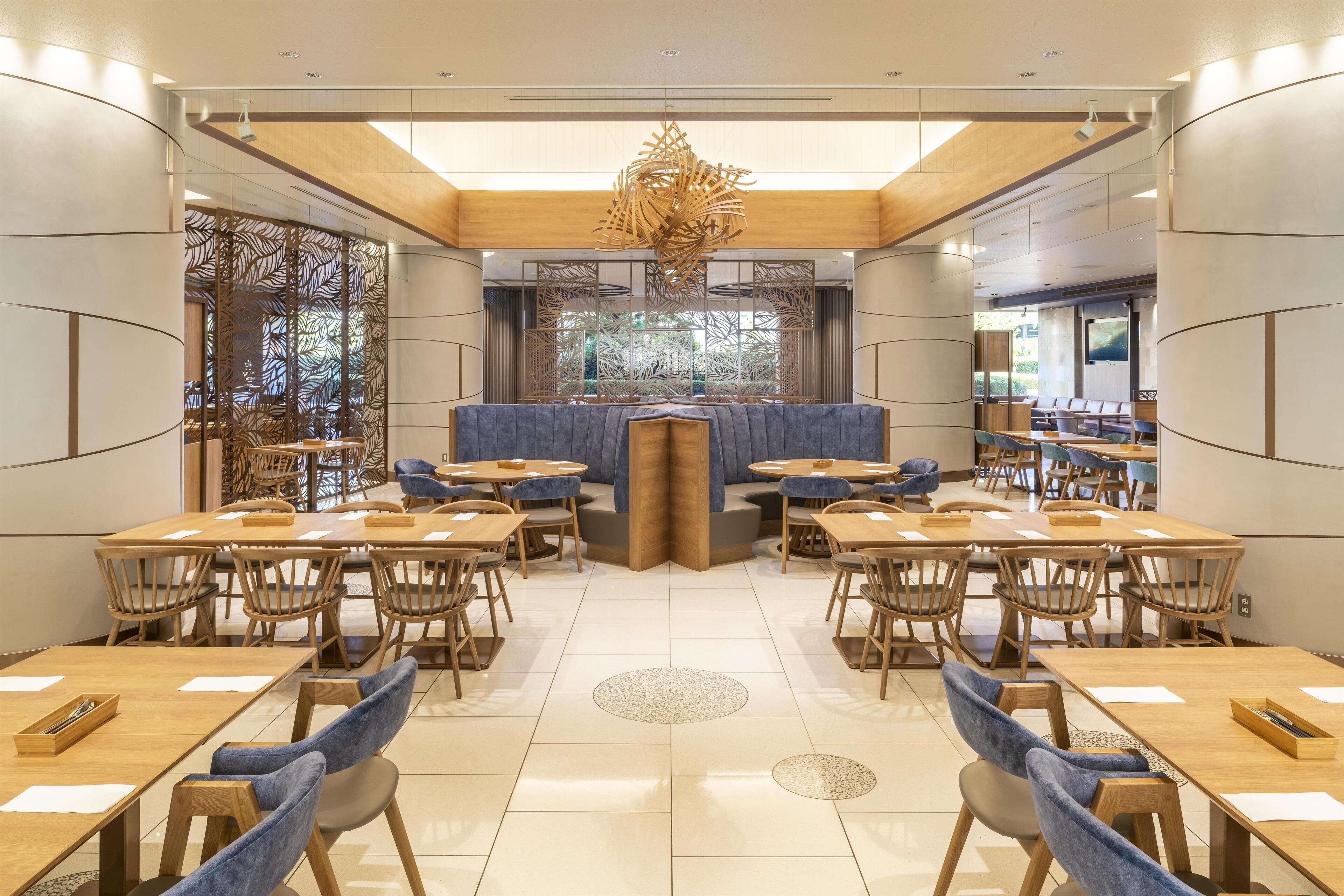 A modern dining area with wooden tables and chairs, a central seating area, and a decorative ceiling light.