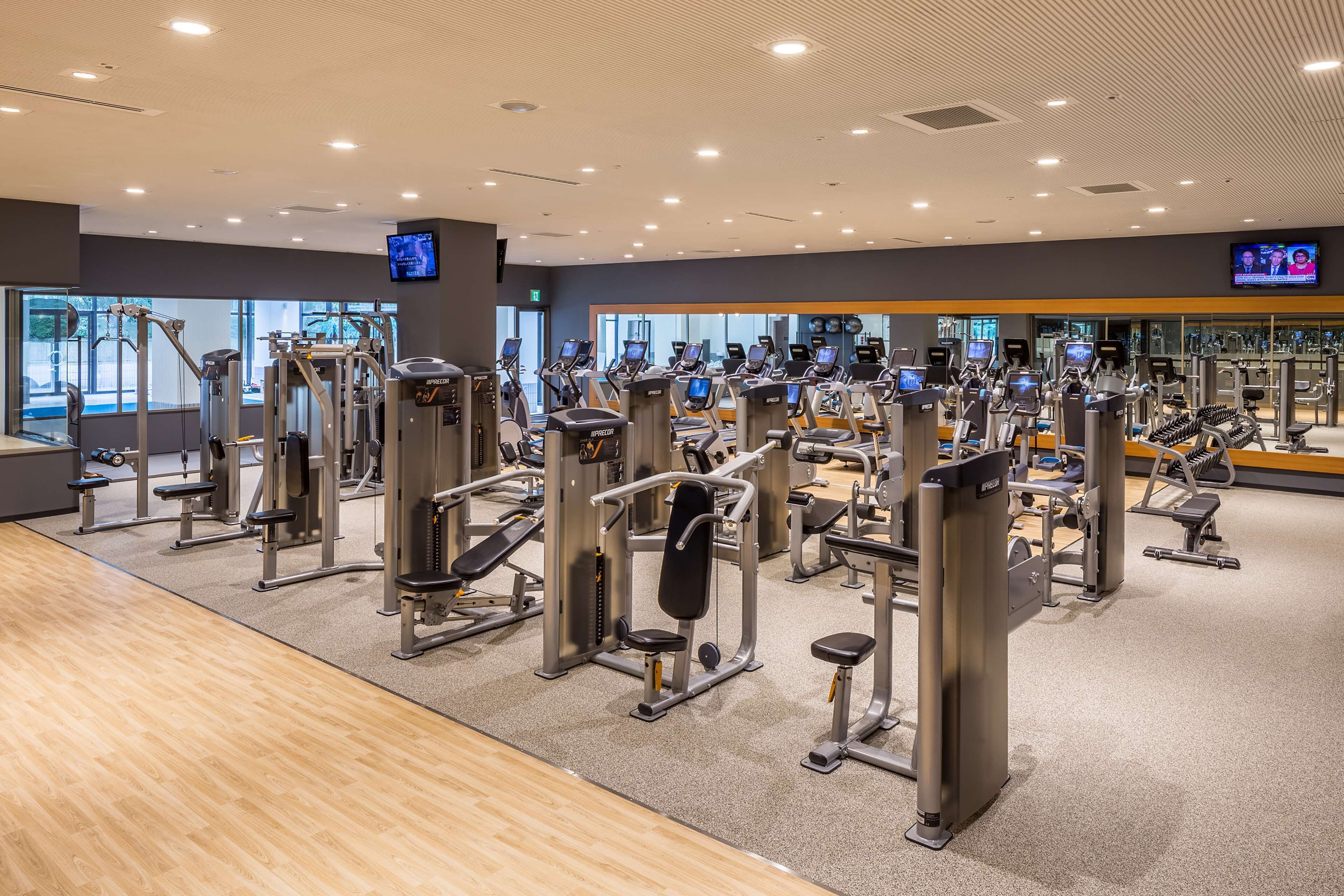 A gym with various exercise machines, a large mirror, and a television screen.