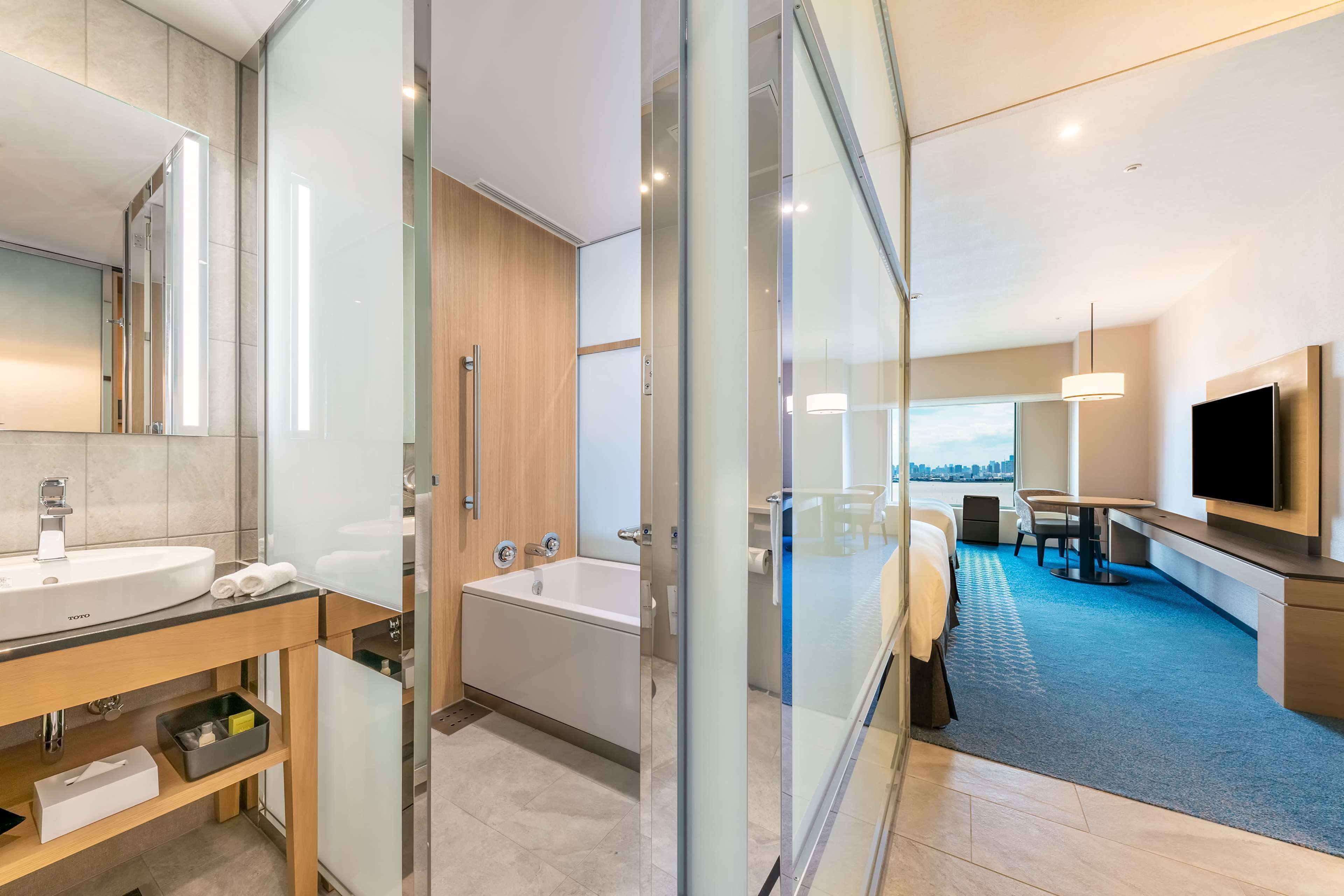 Un baño de hotel moderno con cabina de ducha de vidrio, bañera y tocador con lavabo y espejo.