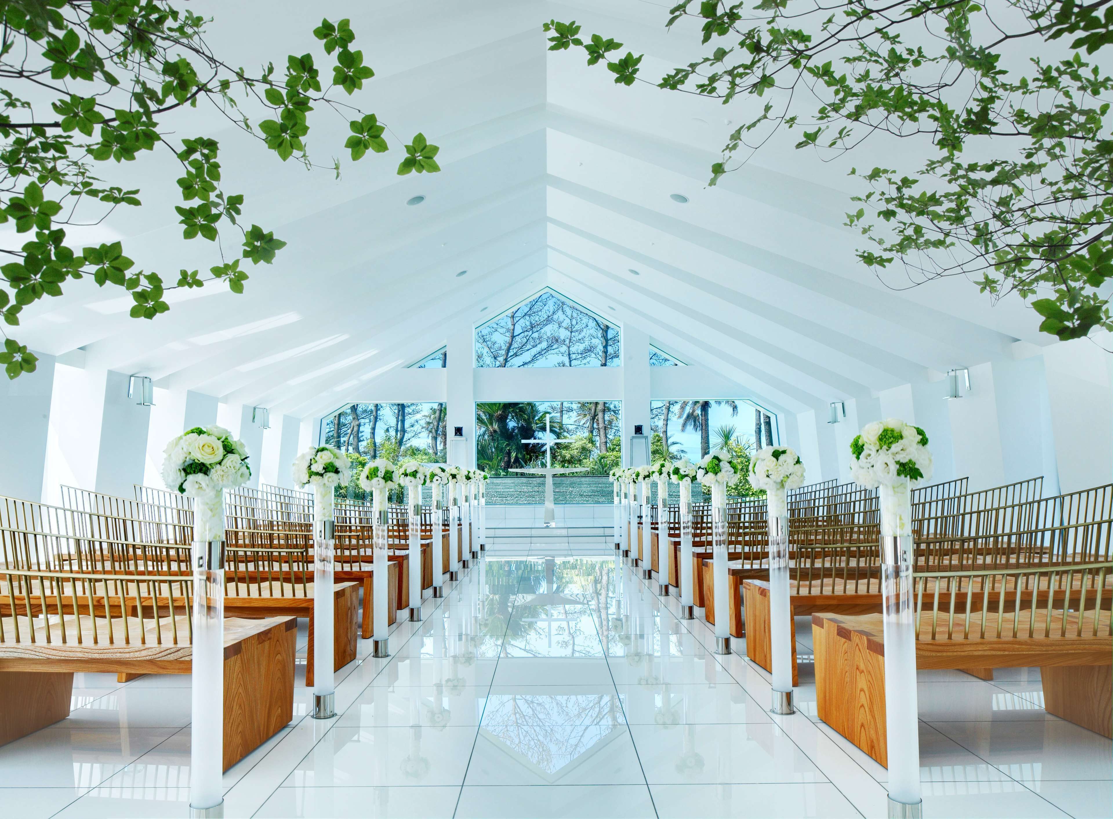A modern church interior with rows of wooden pews, white columns, and large windows.