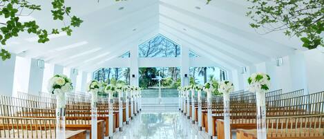 A modern church interior with rows of wooden pews, white columns, and large windows.