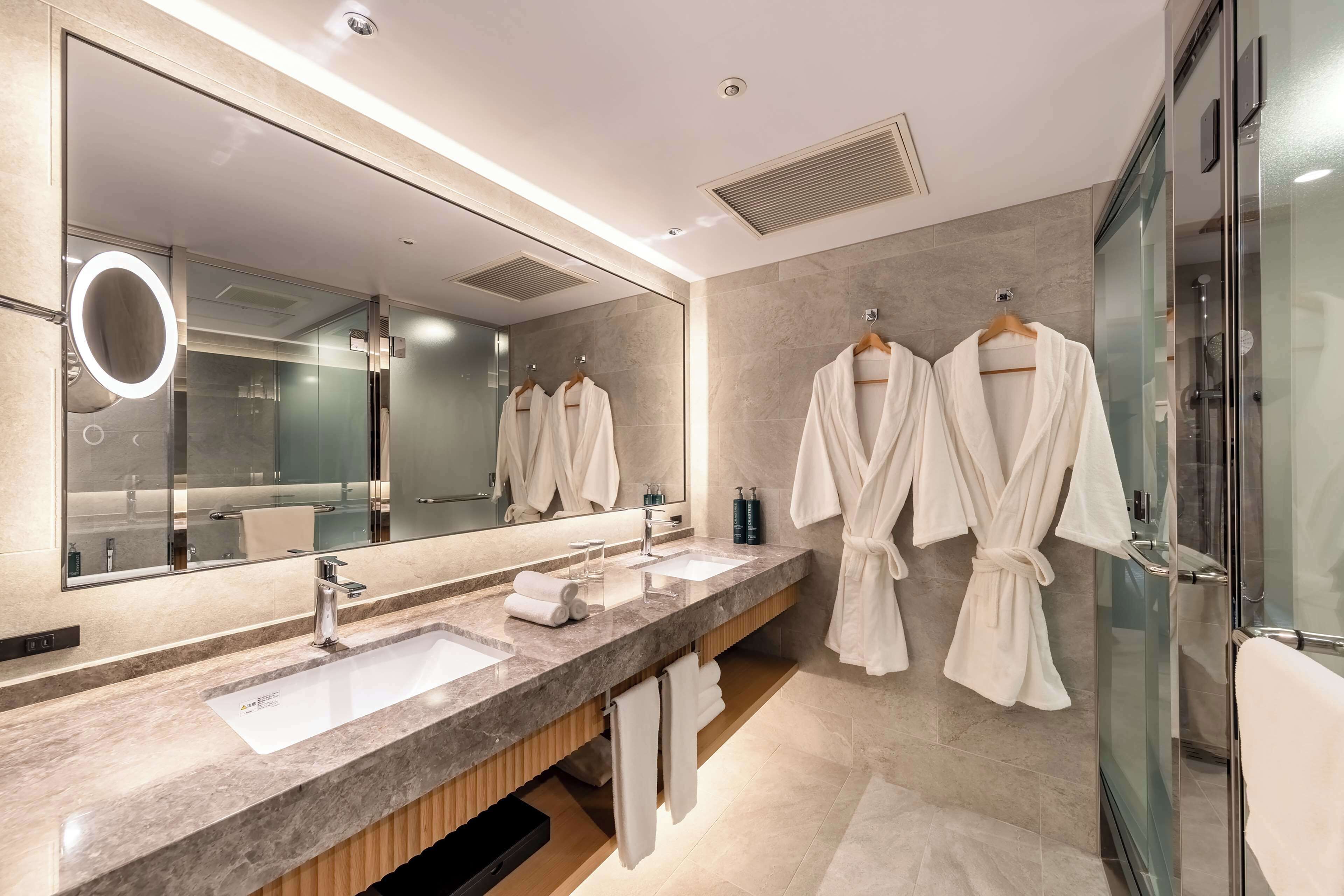 A modern bathroom with two sinks, a large mirror, and two white robes hanging on hooks.