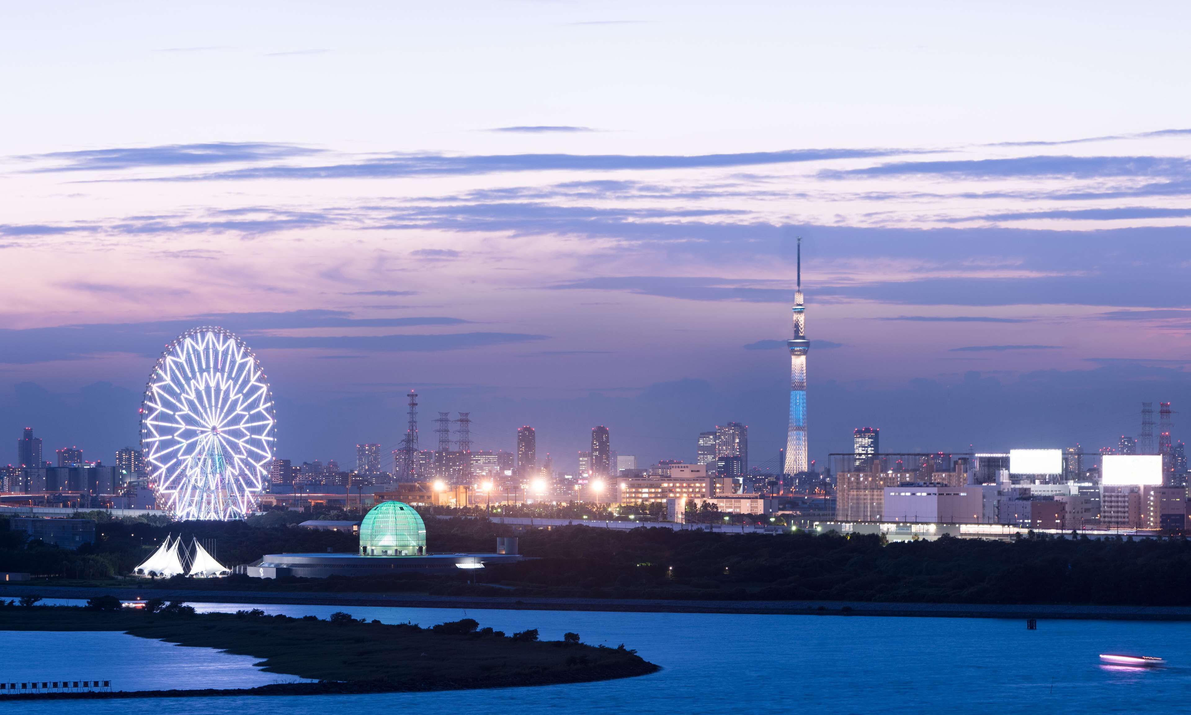 A cityscape with a prominent tower, a large illuminated wheel, and a dome structure.