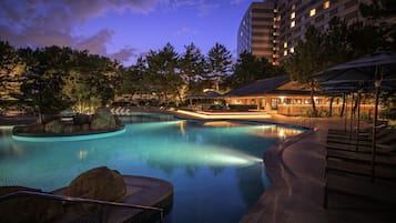 A swimming pool with lounge chairs and umbrellas, surrounded by trees and a building.
