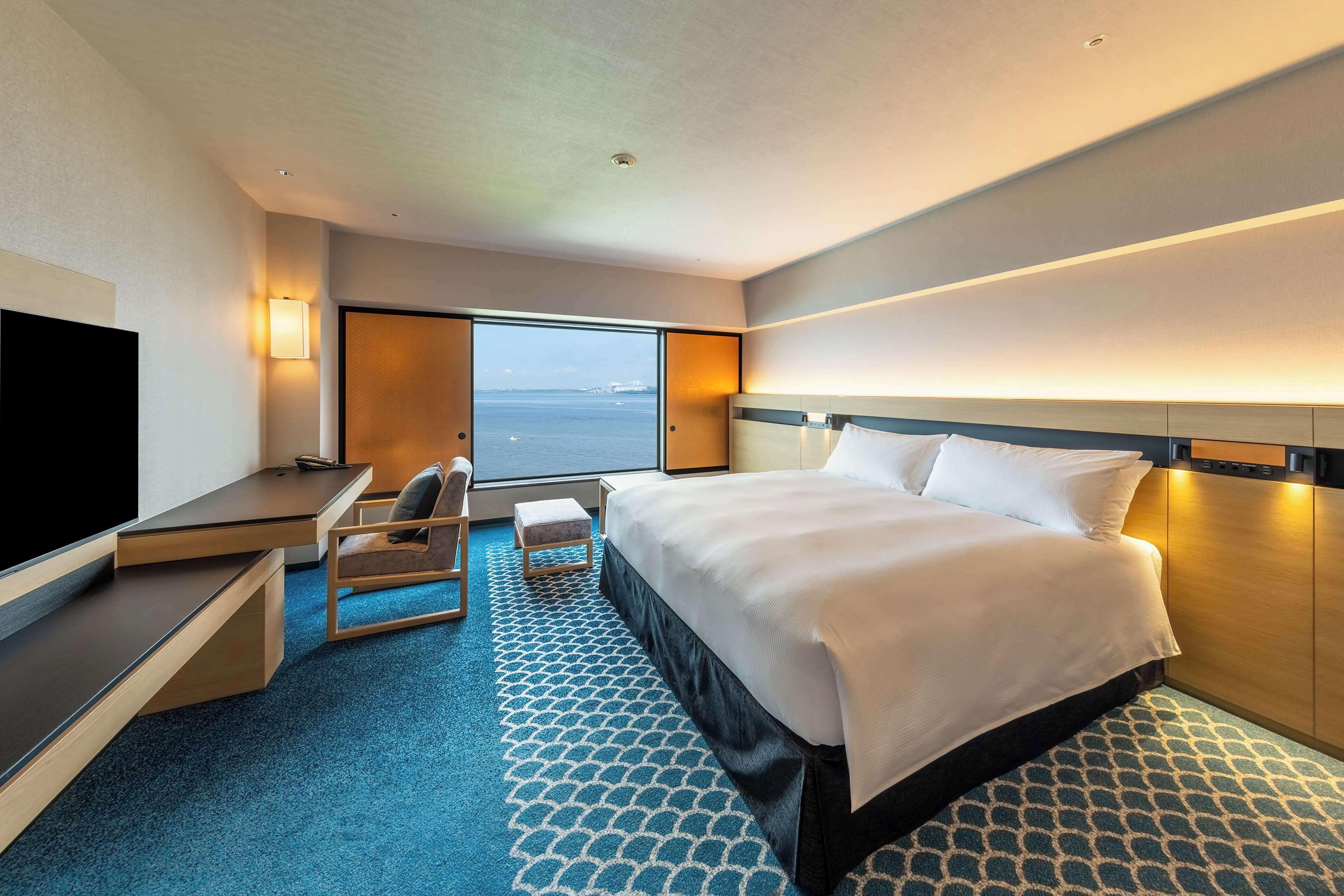 Habitación de hotel con una cama grande, un escritorio, una silla, un televisor y una ventana con vista al mar.