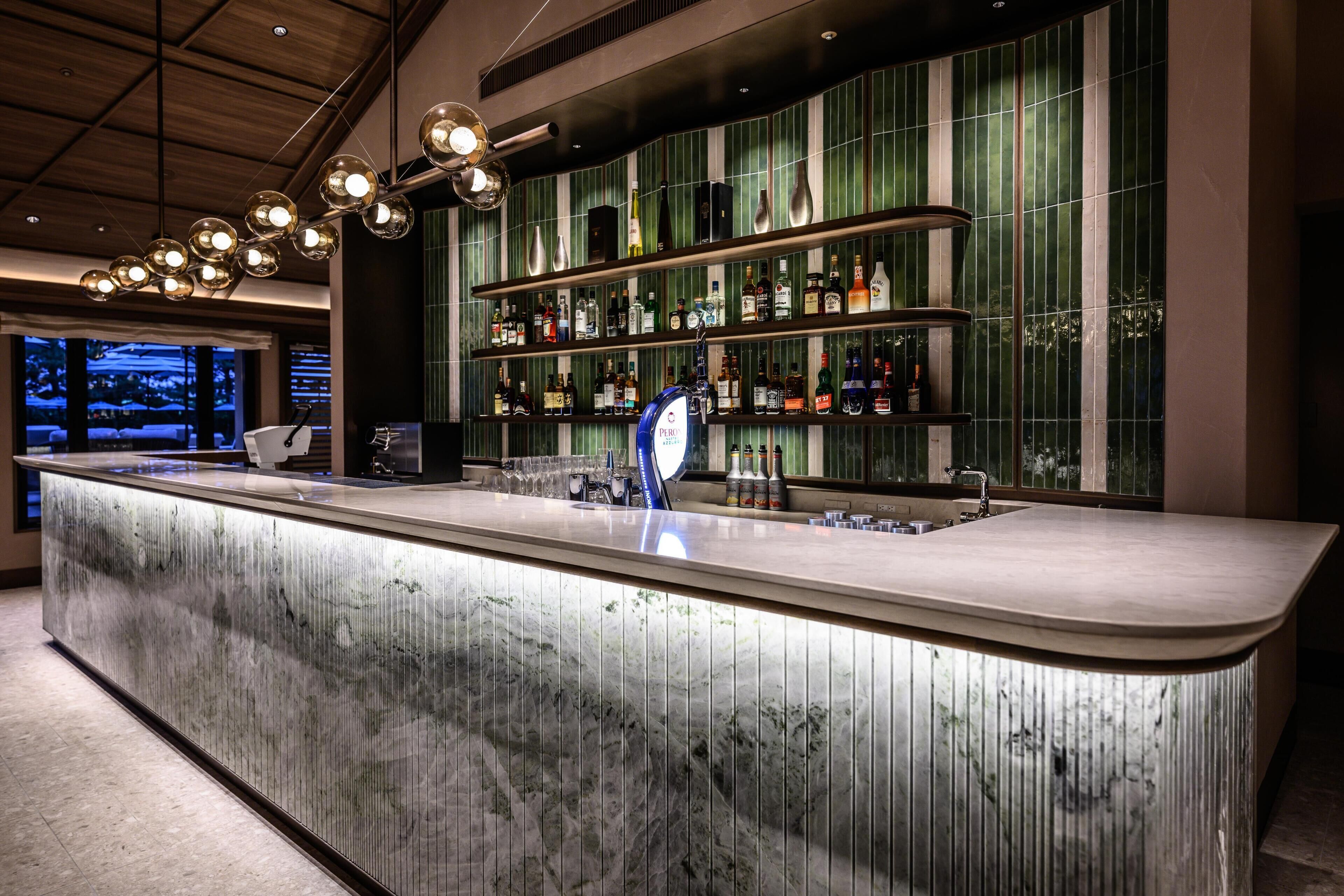 A bar area with a marble countertop, shelves of liquor bottles, and a modern light fixture.