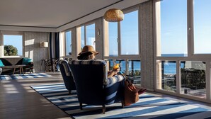 A spacious room with large windows, a blue and white striped rug, and a view of the ocean.