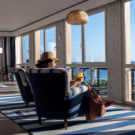 A spacious room with large windows, a blue and white striped rug, and a view of the ocean.