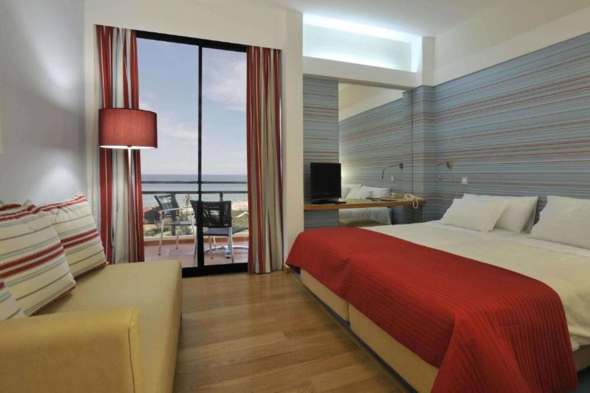 A hotel room with a large bed, a sofa, a TV, and a balcony with a view.