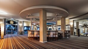 A modern hotel lobby with a curved ceiling, a bar area with stools, and a patterned carpet.